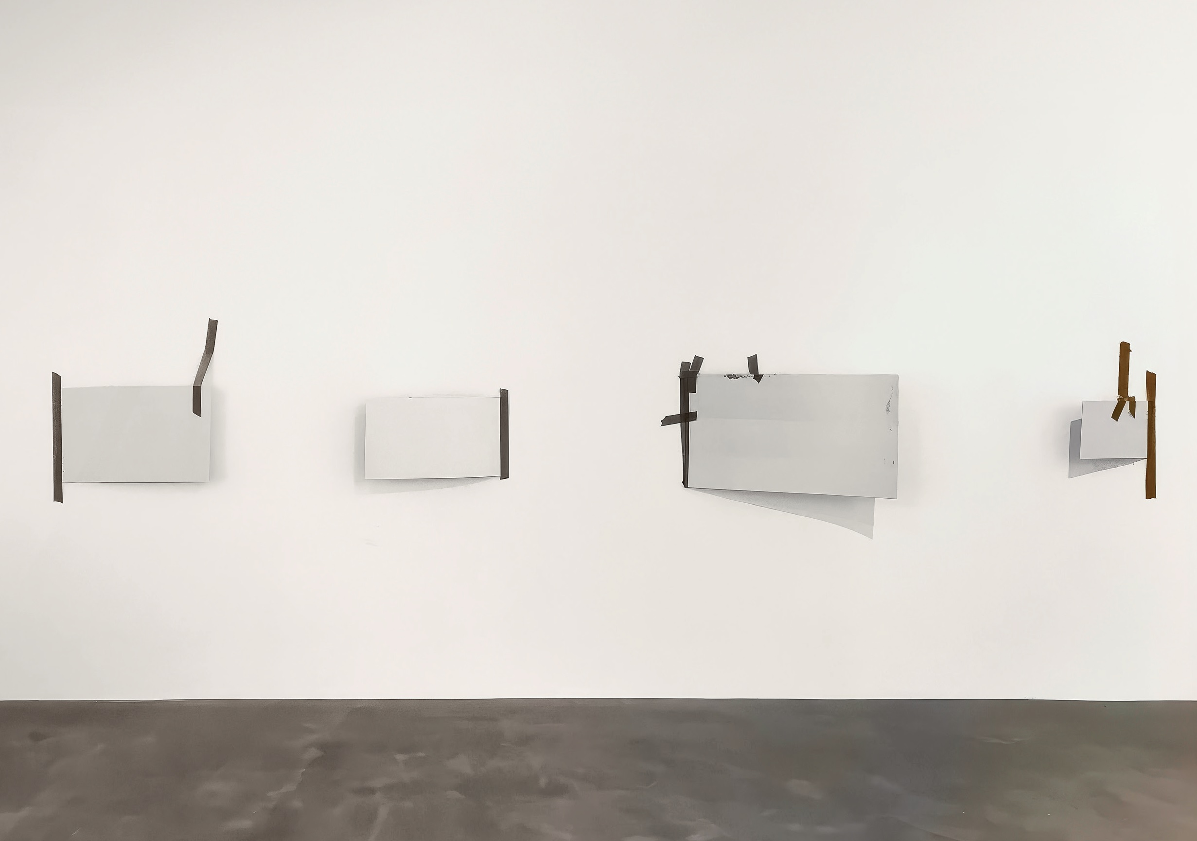 vier Skulpturen hängen an der Wand. Weisse Platten mit dunklem Klebeband