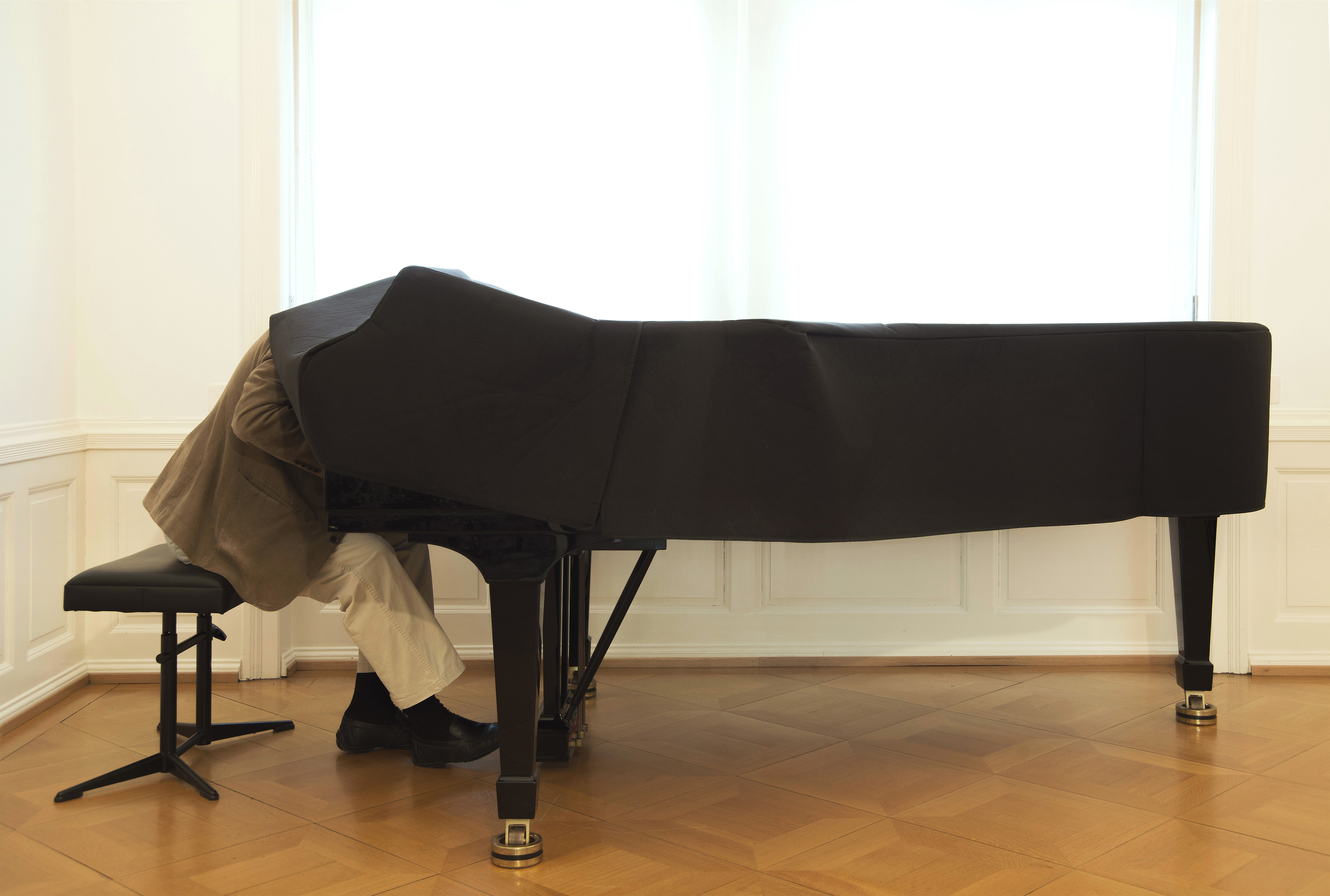 Eine Person sitzt an einem Flügel und steckt mit ihrem Oberkörper in der Stoffhülle des Instruments