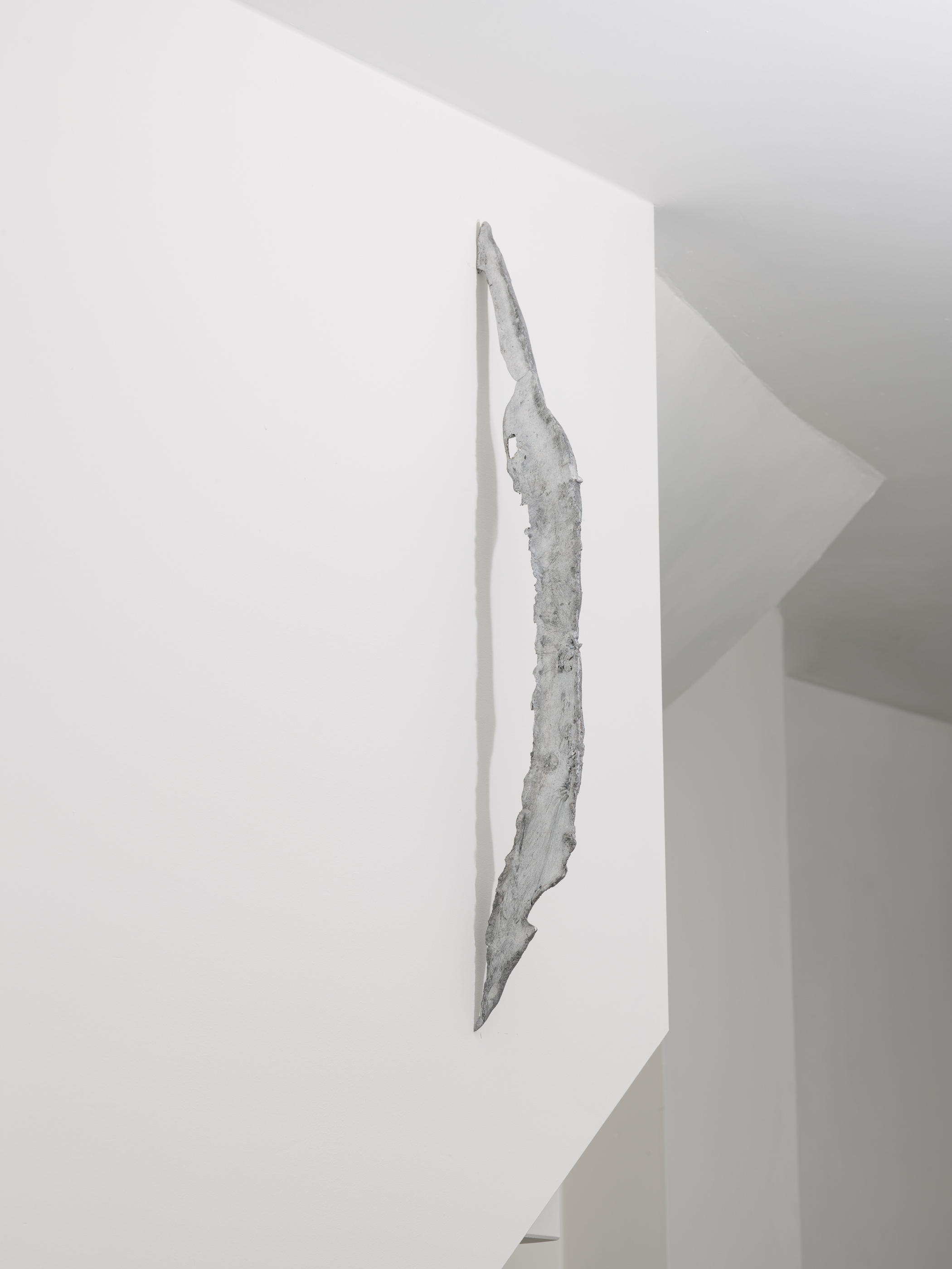An einer weissen Wand hängt eine weiss-gräuliche Skulptur.