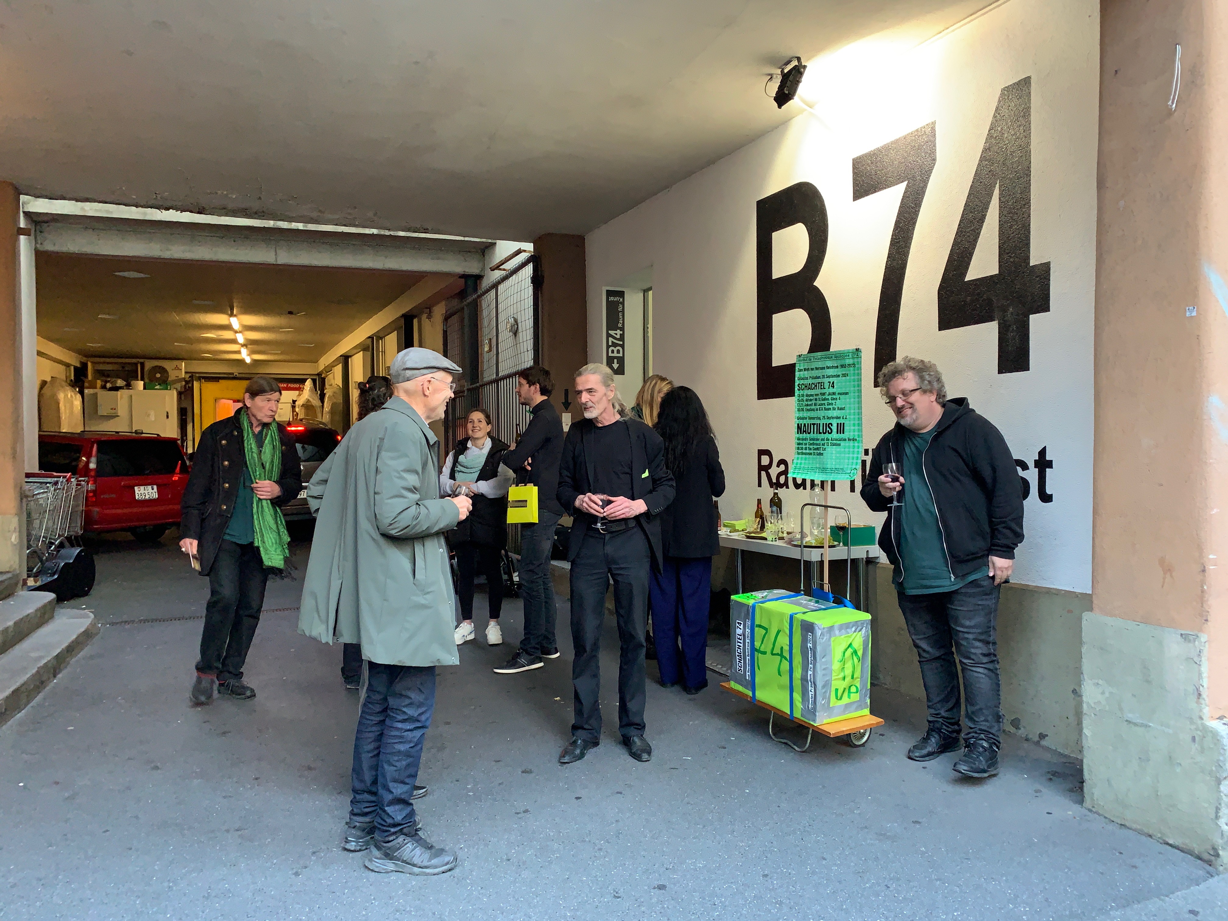 Mehrere Personen stehen vor dem Eingang der Galerie B74 und halten Gläser in der Hand.