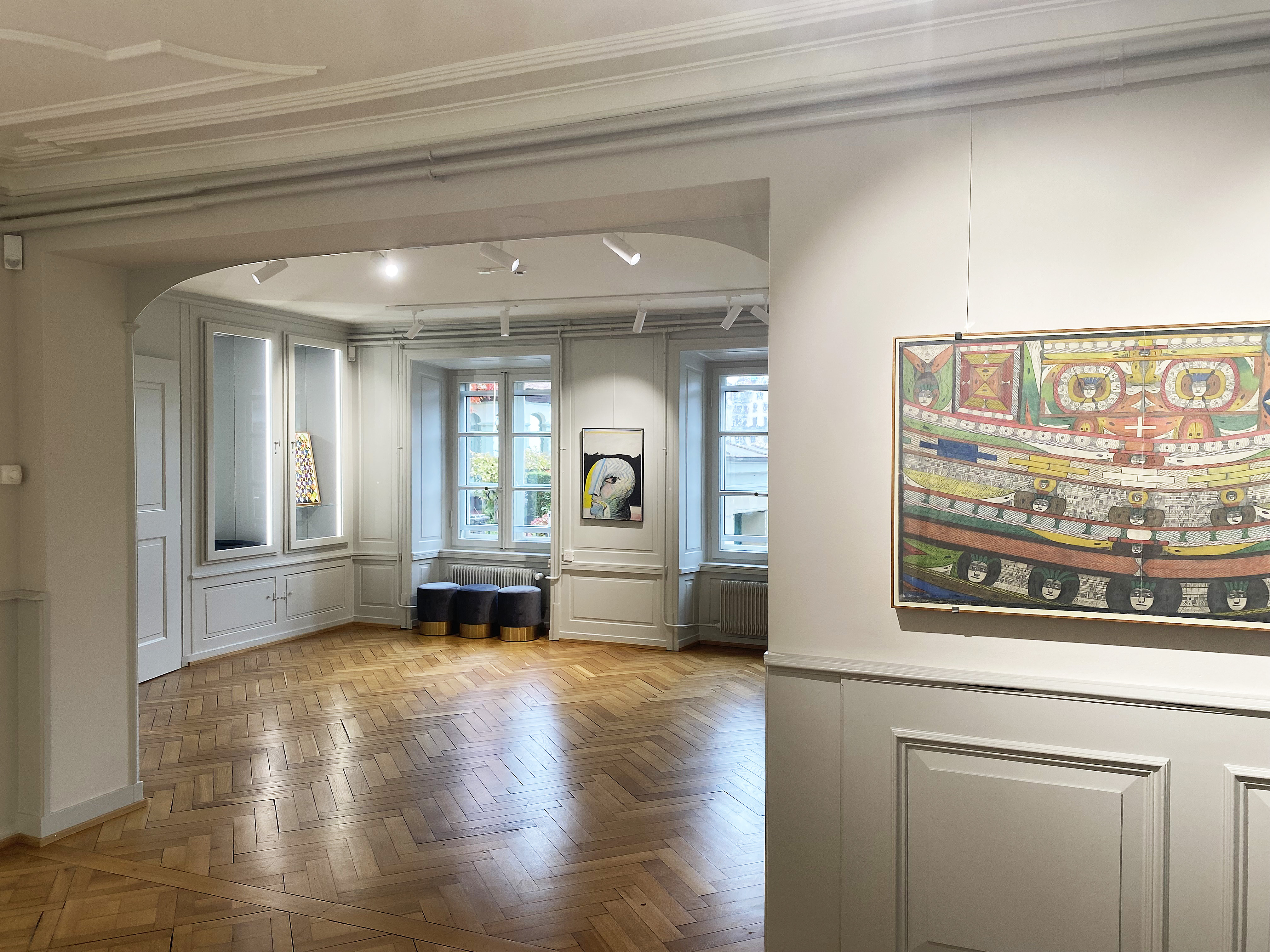 Ein Raum mit Parkettboden. An der Wand hängen beleuchtete Malereien
