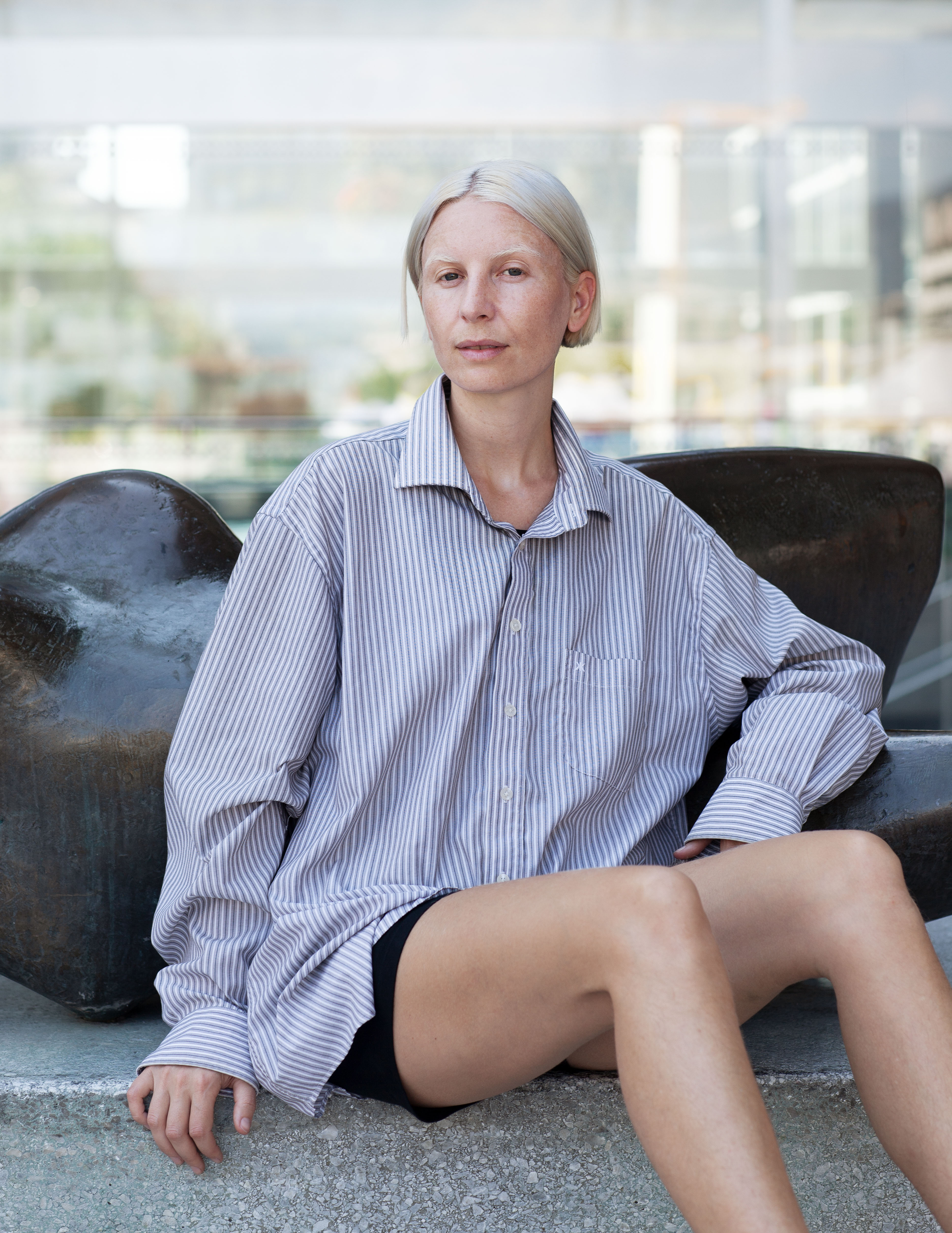 Eine Person in blauem Streifenhemd und sehr hellblondem Haar sitzt auf einem Sofa.