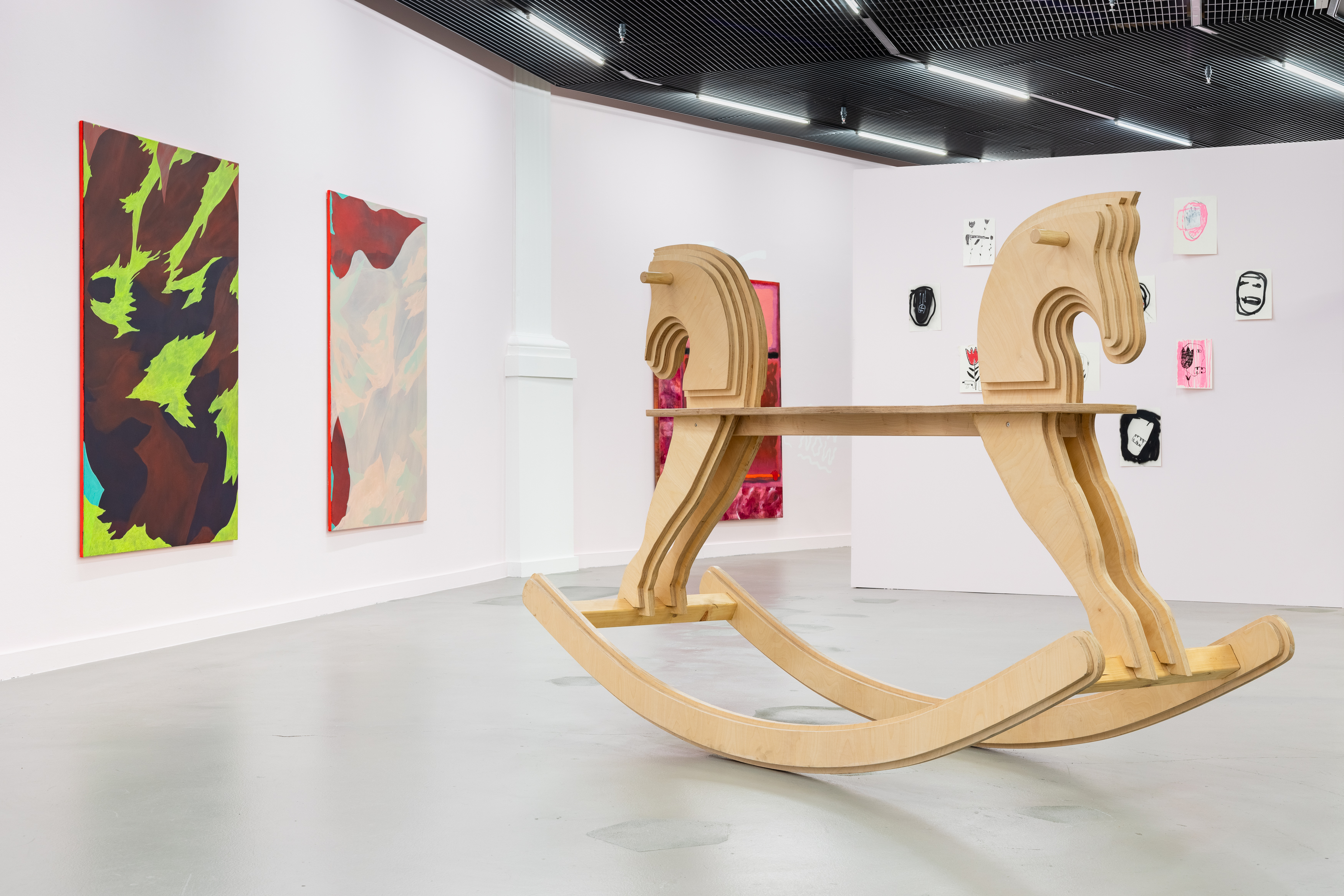Ausstellungsansicht «Love» Kunsthalle Luzern, 2025 Foto : Kilian Bannwart, 2025. Ein gigantisches, zweiseitiges Schaukelpferd, dahinter grosse, bunte Malereien