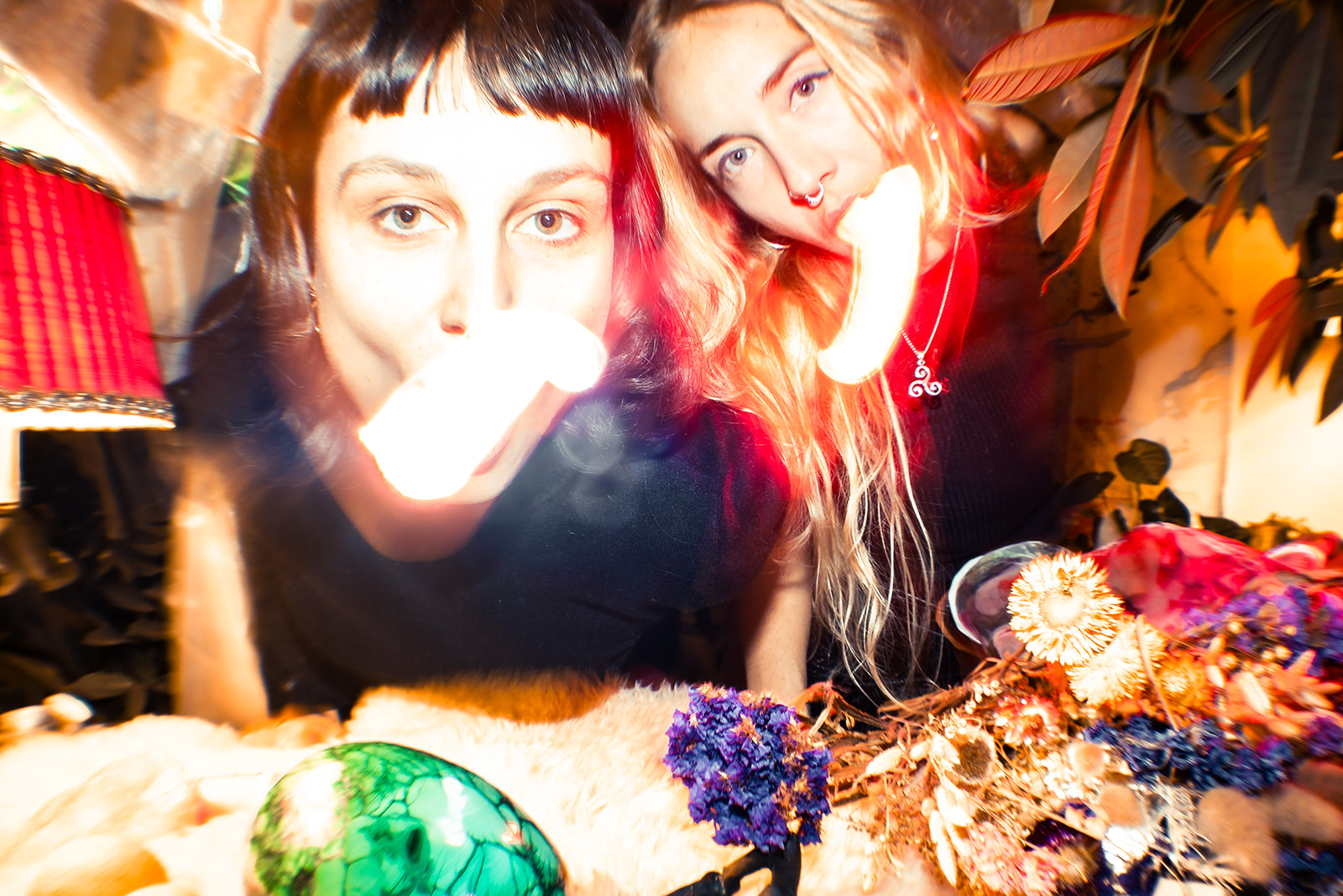 Laura Jana Luterbach & Naira Ramos, 2025 Foto : Leon Maria Plecity - Die zwei Künstlerinnen stehen vor einem Tisch mit bunten Objekten und Blumen