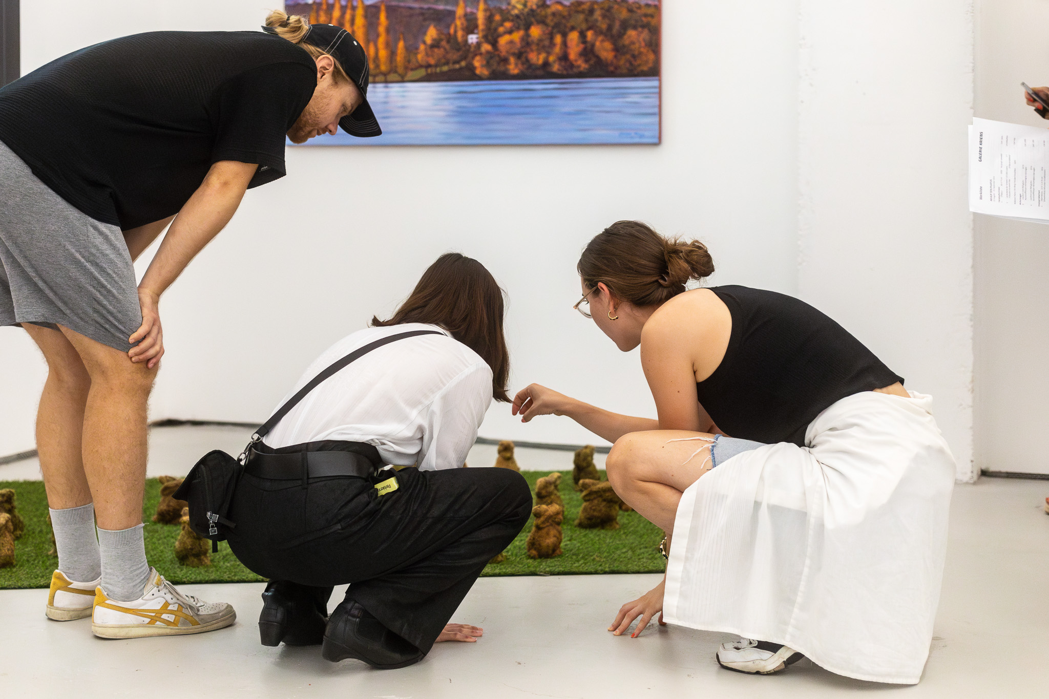 Foto Rundgang 2024: Mario Grossenbacher Drei junge Menschen bücken sich über eine Miniaturwelt auf dem Boden eines Ausstellungsraumes