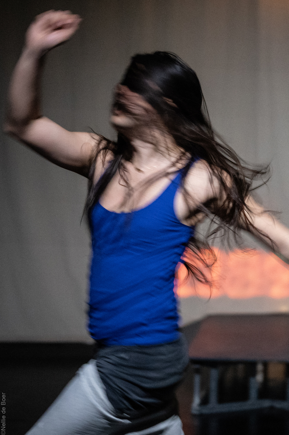 Performer:in Yadin Bernauer - Person mit langem Haar über dem Gesicht bewegt sich und trägt ein blaues Träger-Oberteil.