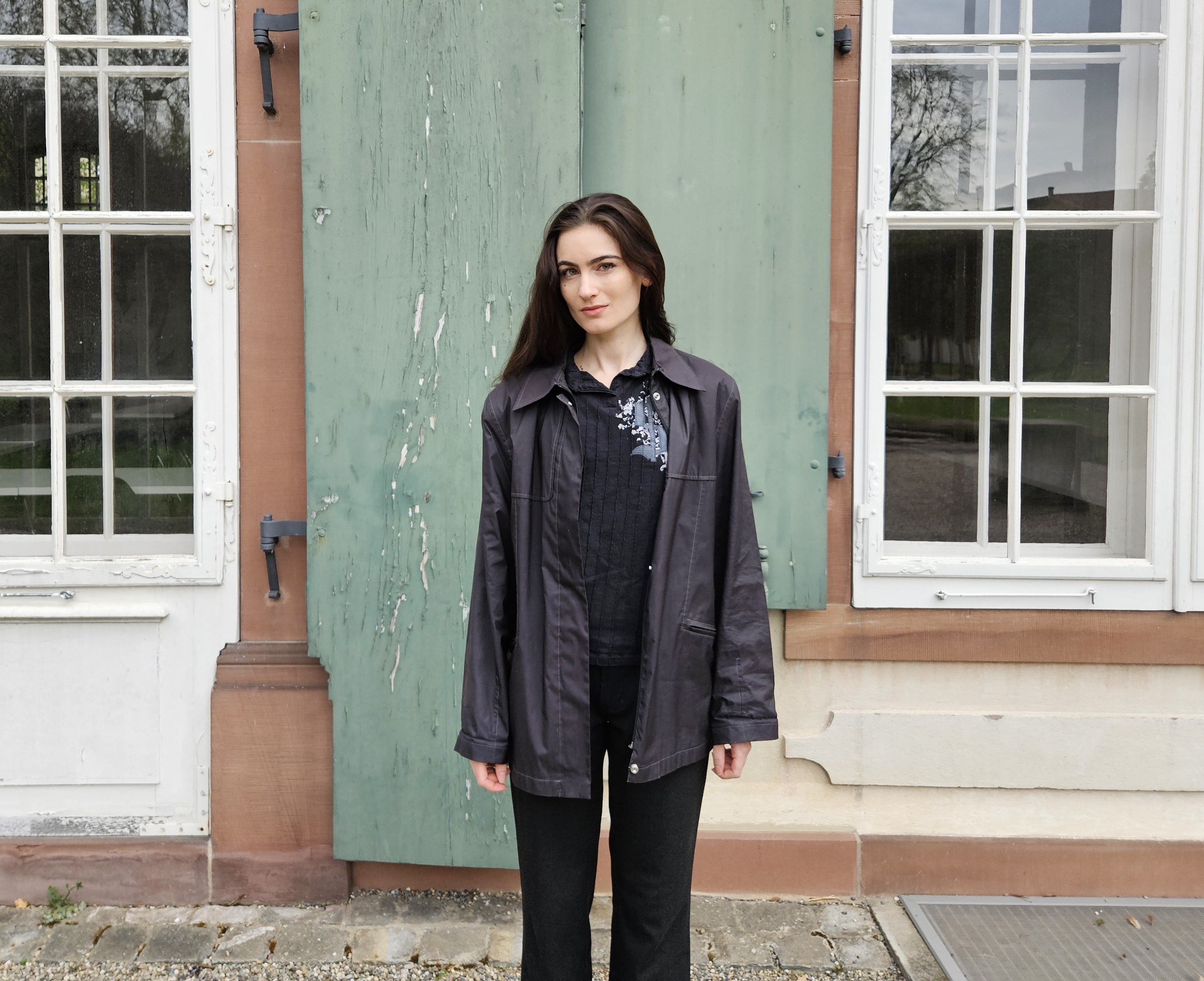 Eleonora Bitterli steht vor einer Hausfassade und schaut in die Kamera. Sie trägt ein koplett schwarzes Outfit.