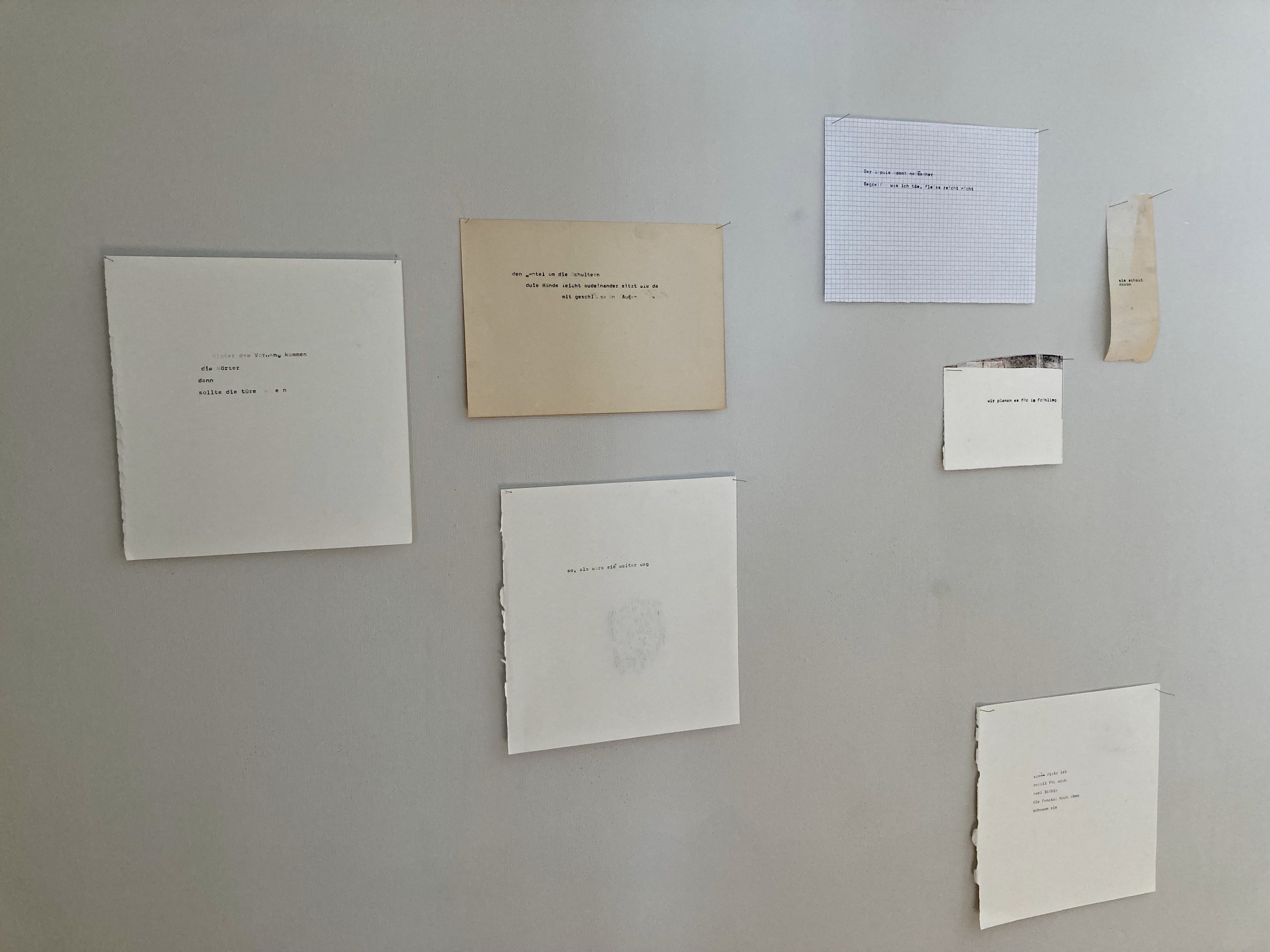 Einige verschieden grosse Papier-Stücke an die Wand geklebt. Es hat Text darauf.