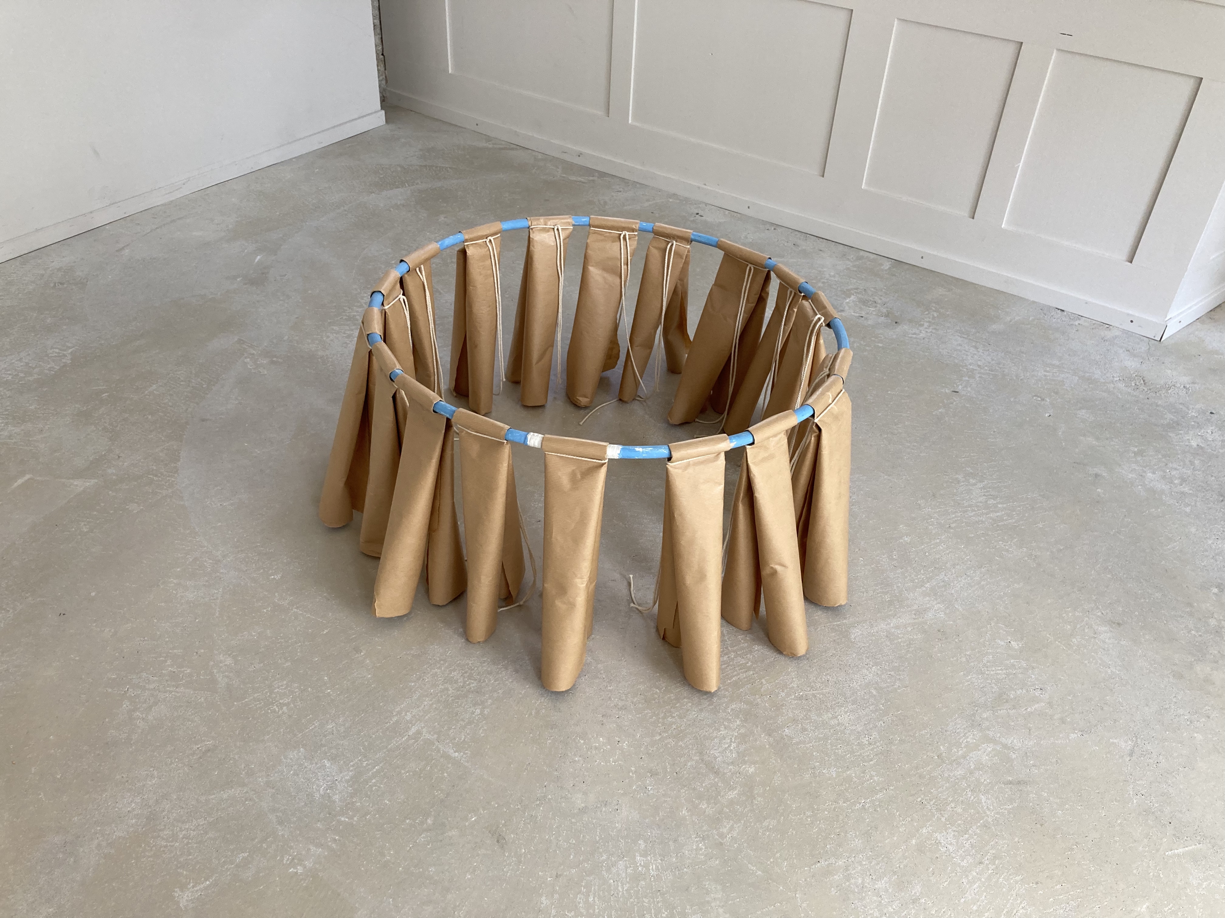 Skulpturales Objekt aus Papier und einem Reifen. Das Papier trägt den Ring und stützt ihn vom Boden ab 