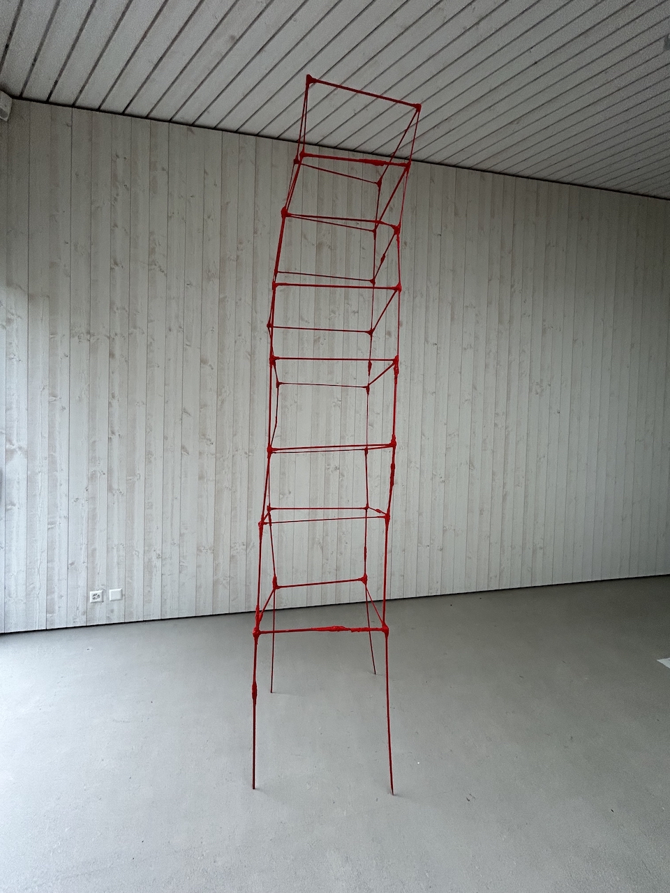 Eine Turm-Skulptur aus 126 roten Stäben in einem leeren Ausstellungsraum
