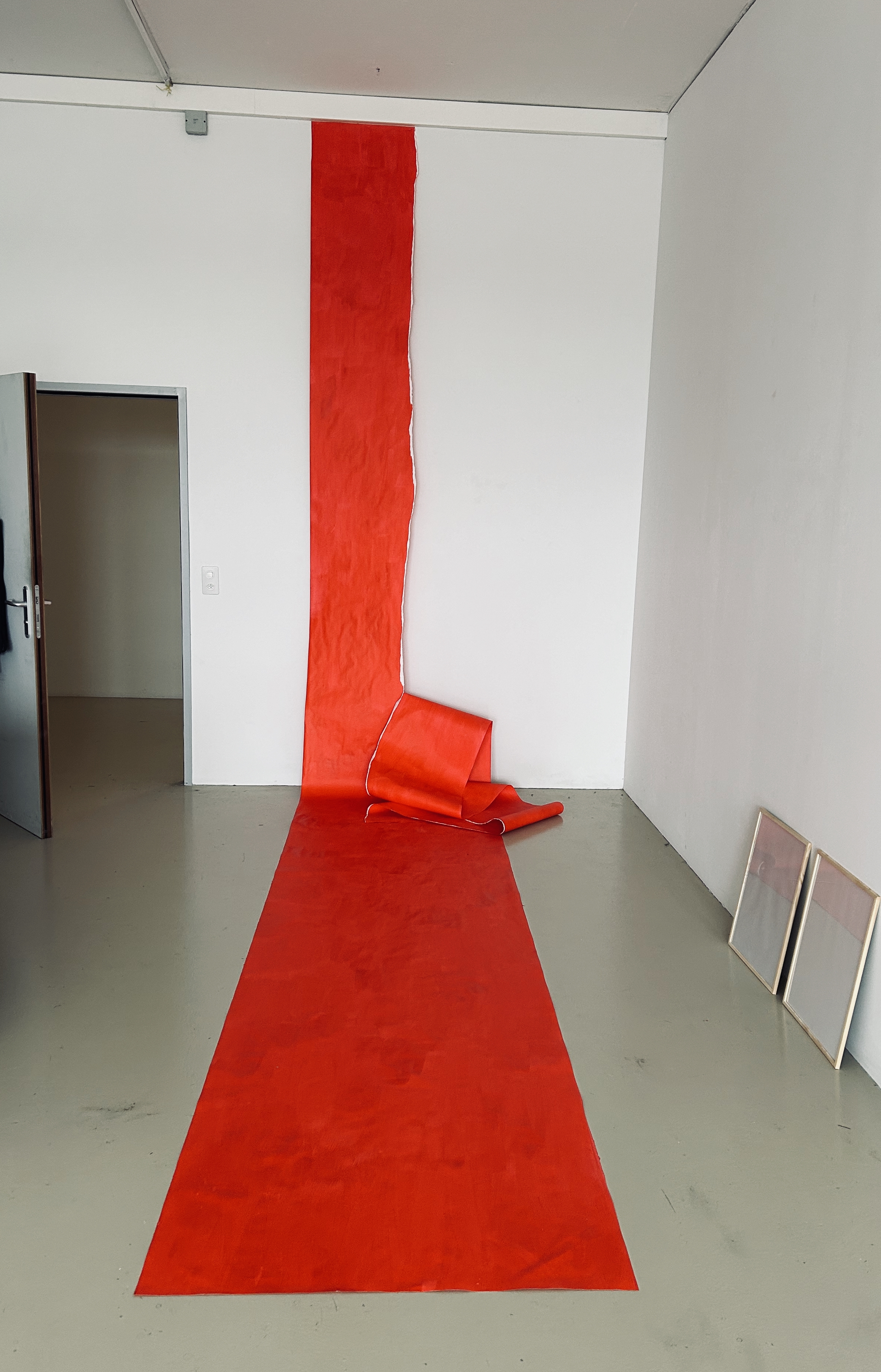 ein langes, rotes Stück Papier mit einem langen Riss darin hängt von der Decke, der Wand und dem Boden entlang