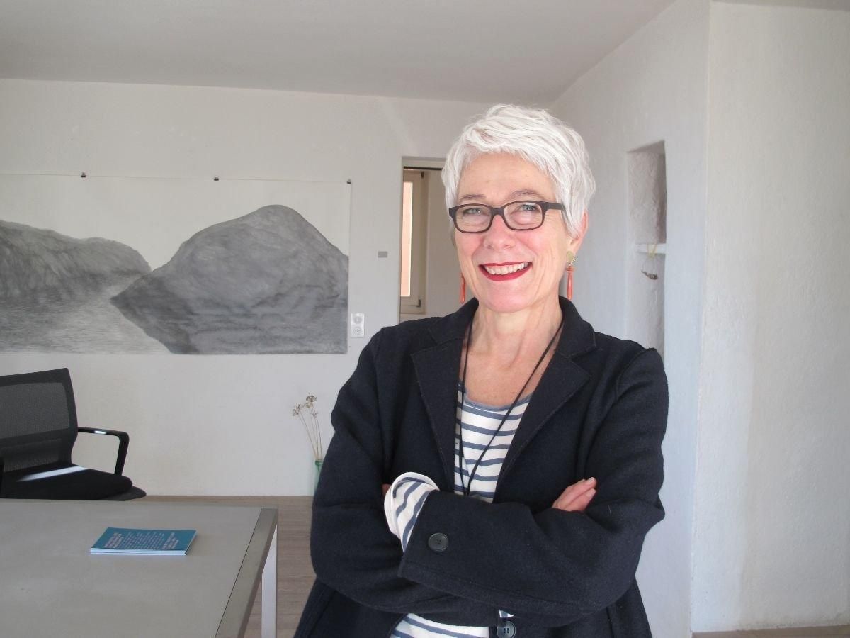 Monika Feucht steht mit verschränkten Armen und lächelnd vor einem Kunstwerk