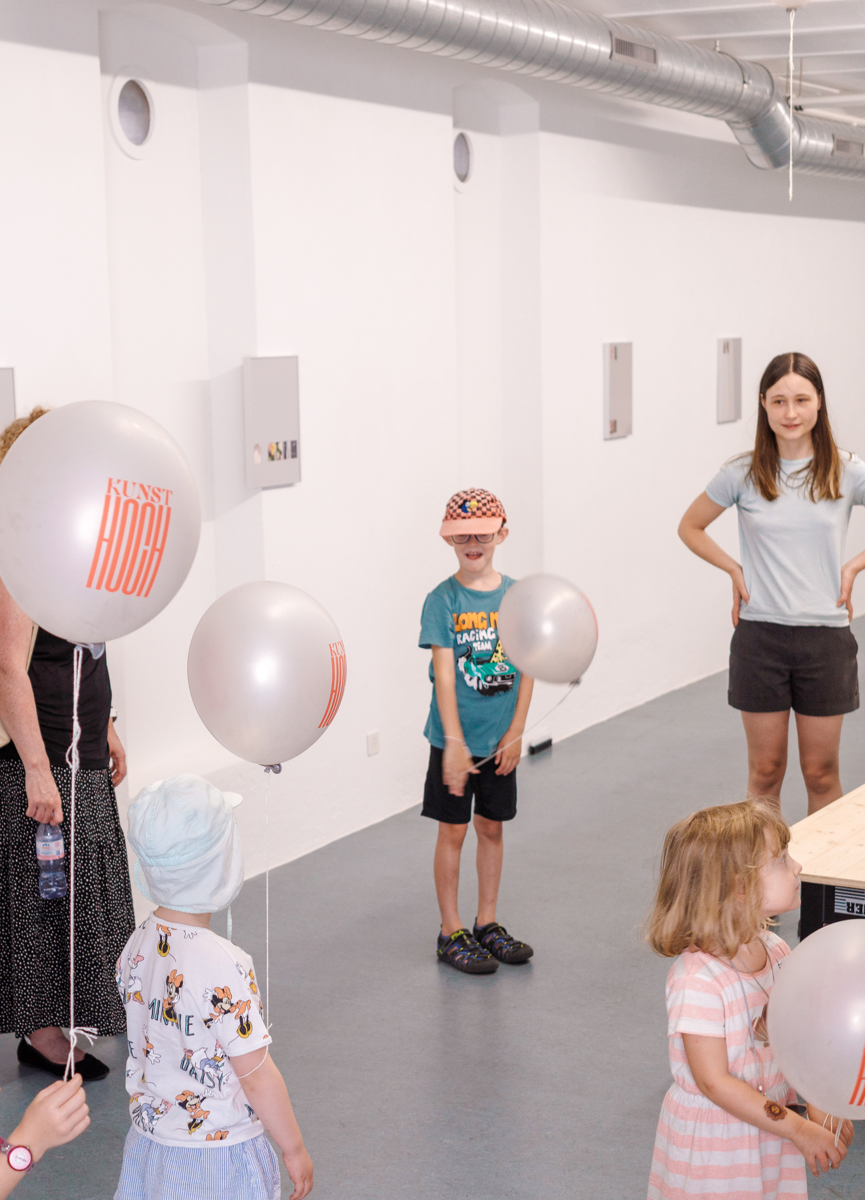 Sophie Nadler steht mit Kindern im Ausstellungsraum. Es schweben mehrere Kunsthoch-Ballons im Raum
