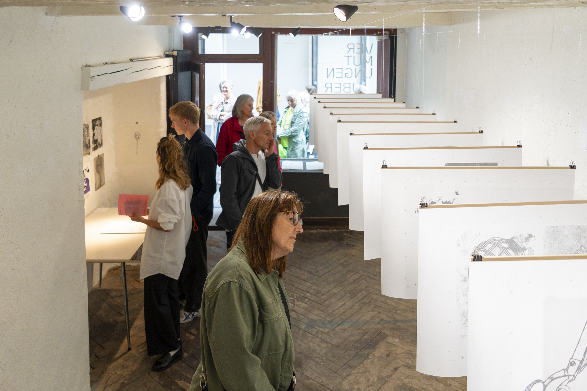 Foto von Mario Grossenbacher Menschen schauen sich eine Ausstellung mit aufgereihten Zeichnungen an, die von der Decke hängen