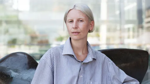 Eine Person in blauem Streifenhemd und sehr hellblondem Haar sitzt auf einem Sofa.