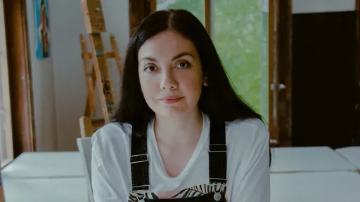 Amalia Maciuca hat langes, dunkles Haar und trägt eine Arbeiter-Latzhose über einem weissen Shirt.