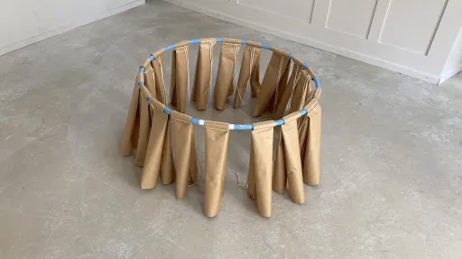 Skulpturales Objekt aus Papier und einem Reifen. Das Papier trägt den Ring und stützt ihn vom Boden ab 