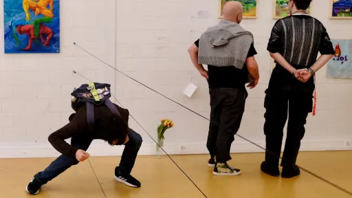 Eine Person bückt sich unter einem Seil hindurch, das quer über den Raum gespannt ist.