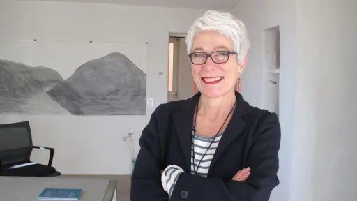 Monika Feucht steht mit verschränkten Armen und lächelnd vor einem Kunstwerk