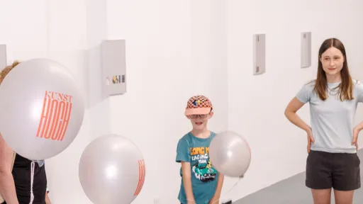 Sophie Nadler steht mit Kindern im Ausstellungsraum. Es schweben mehrere Kunsthoch-Ballons im Raum