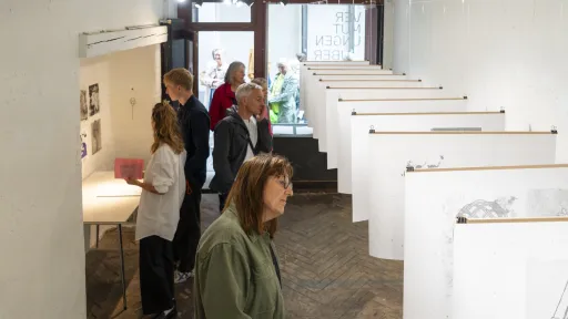 Menschen schauen sich eine Ausstellung mit aufgereihten Zeichnungen an, die von der Decke hängen