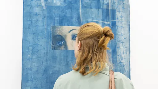 Eine Person blickt auf eine blaue Druckgrafik mit einem abgebildeten Augenpaar